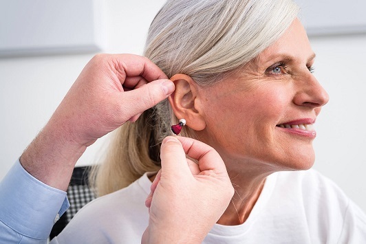 Ältere Frau bekommt von einem Hörakustiker ein modernes Hörgerät ins Ohr eingesetzt.